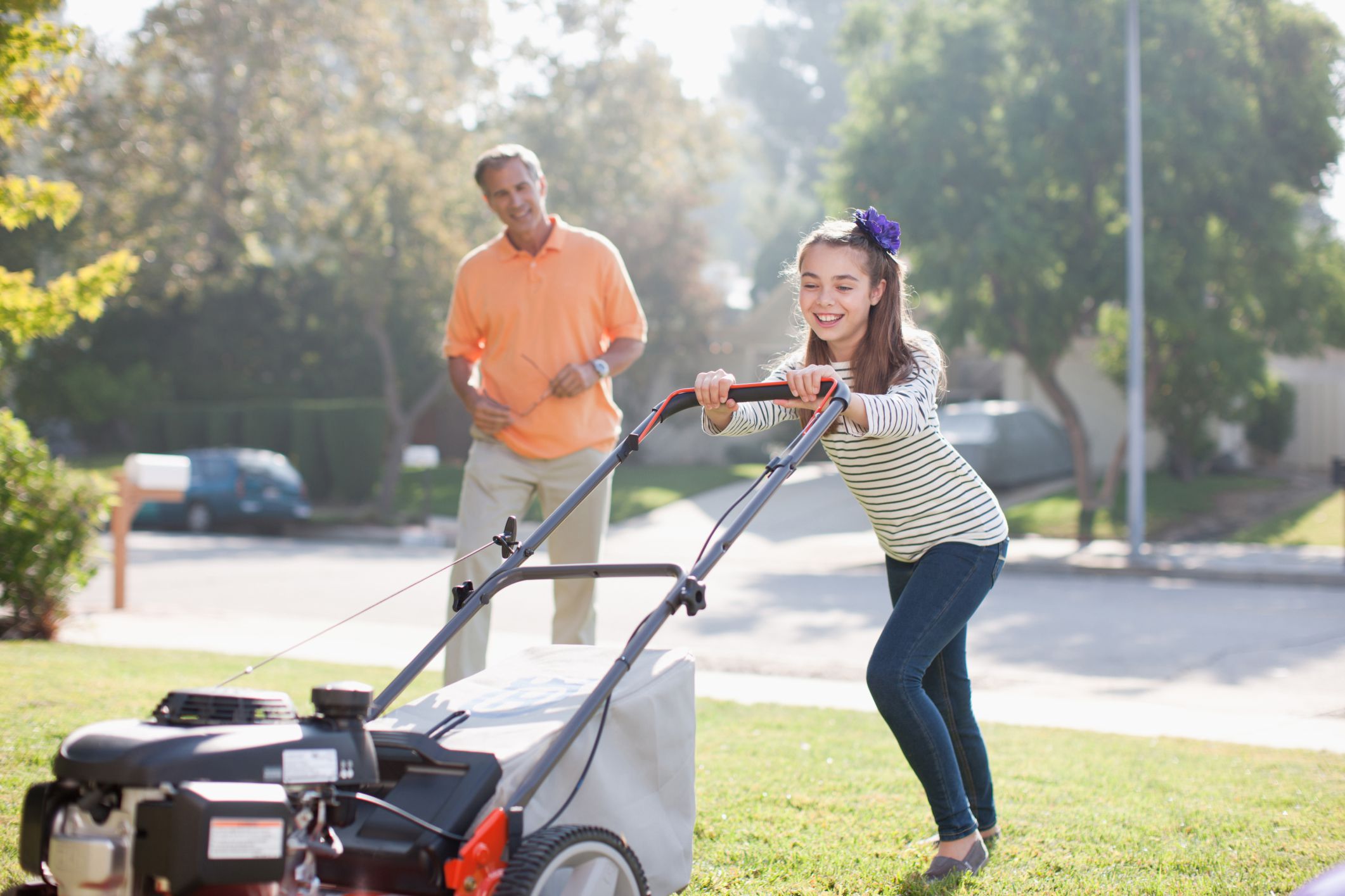 Little girl mowing lawn with assistence from her dad